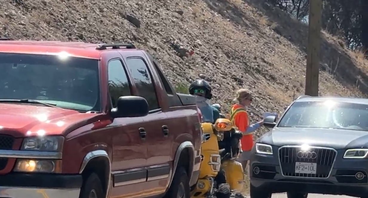 A person in a high-viz vest speaks to a driver in a car sitting in a lineup of cars