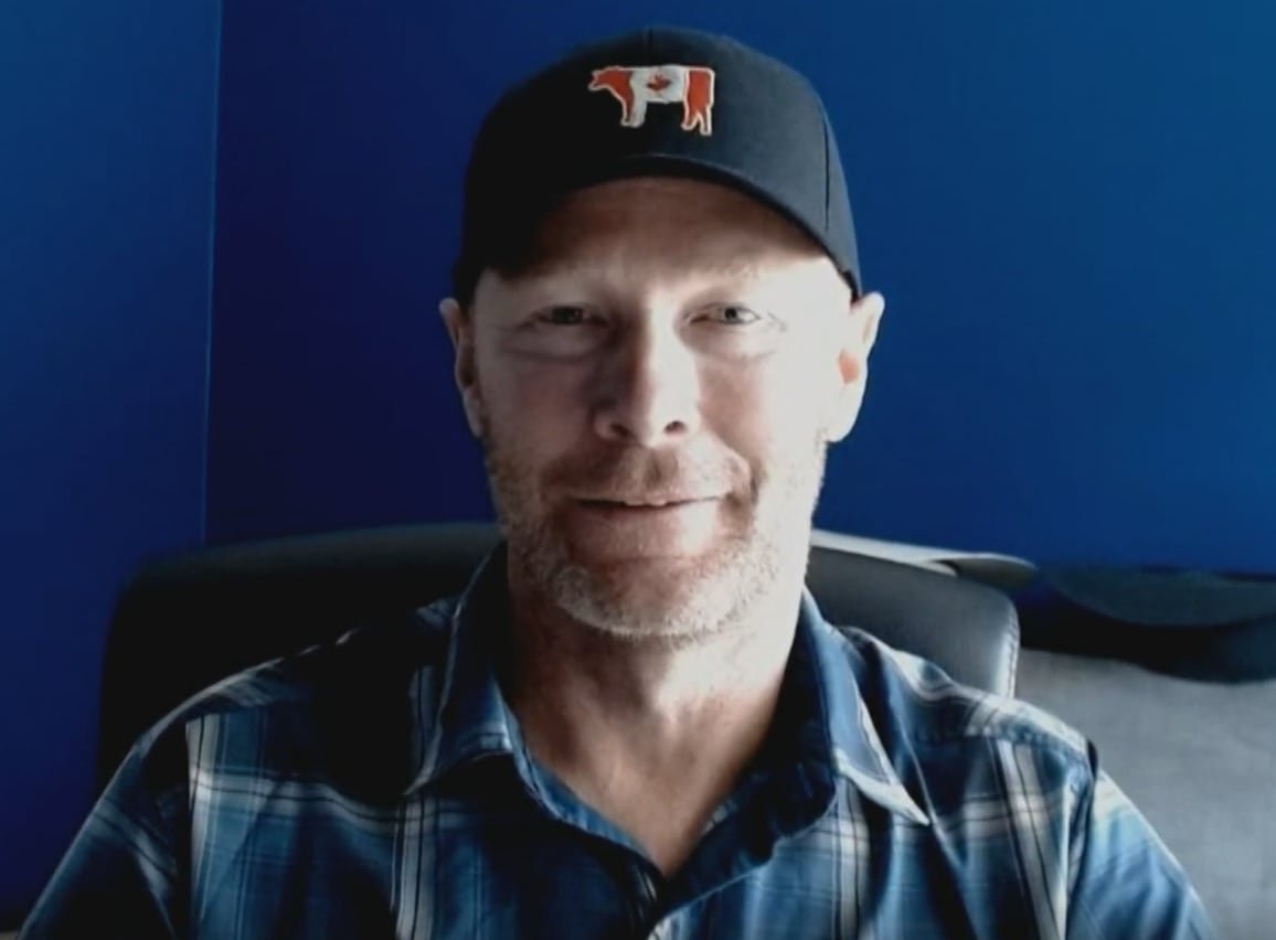 A man in a cap with a Canadian flag shaped like a cow does an online interview.